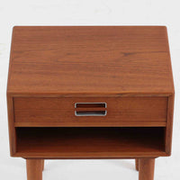 デンマーク製のサイドチェストで、シンプルなボックス構成にチーク材の豊かな風合いが映える北欧ビンテージらしい一台です。オープンスペースは本や小物の収納に便利で、引き出しには金属フレームを組み合わせたユニークな取手がアクセントとして効いています。丸みを帯びた角や細く伸びたテーパードレッグが軽快な印象を与え、ベッドサイドやソファ横でのサイドテーブル使いにも最適。経年変化の味わい深い木肌が空間に温かさと上質さを添えます。