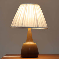 Per Lindemann SchmidtがPalshusのために手掛けたモデル「PL-5 SL 2」は、均整の取れたシルエットと滑らかに焼き締められたマットブラウンの陶肌が静かな存在感を放つテーブルランプで、首元にほんのり入る明るい釉薬のグラデーションが柔らかな表情を添える北欧ビンテージ品です。プリーツシェード越しに広がる落ち着いた灯りはリビングやベッドサイドに心地よい温もりをもたらし、シンプルながら洗練された造形美と経年で深まった風合いを長く楽しめる一台です。