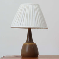 Per Lindemann SchmidtがPalshusのために手掛けたモデル「PL-5 SL 2」は、均整の取れたシルエットと滑らかに焼き締められたマットブラウンの陶肌が静かな存在感を放つテーブルランプで、首元にほんのり入る明るい釉薬のグラデーションが柔らかな表情を添える北欧ビンテージ品です。プリーツシェード越しに広がる落ち着いた灯りはリビングやベッドサイドに心地よい温もりをもたらし、シンプルながら洗練された造形美と経年で深まった風合いを長く楽しめる一台です。