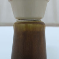 Per Lindemann SchmidtがPalshusのために手掛けたモデル「PL-5 SL 2」は、均整の取れたシルエットと滑らかに焼き締められたマットブラウンの陶肌が静かな存在感を放つテーブルランプで、首元にほんのり入る明るい釉薬のグラデーションが柔らかな表情を添える北欧ビンテージ品です。プリーツシェード越しに広がる落ち着いた灯りはリビングやベッドサイドに心地よい温もりをもたらし、シンプルながら洗練された造形美と経年で深まった風合いを長く楽しめる一台です。