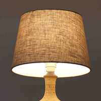 Jette HelleroeがAxellaのために手掛けたこちらのテーブルランプは、砂質の陶肌を生かした素朴で温かみのある質感と、ベース部分にぐるりと施された幾何学的なレリーフ装飾が印象的で、手仕事の風合いが際立つ北欧ビンテージ品です。すらりと立ち上がるシルエットが軽やかなバランスをつくり、リネンシェードを透ける柔らかな灯りがリビングやベッドサイドに落ち着いた雰囲気を添え、経年で深まった土味と装飾の陰影が一点物ならではの魅力を一層引き立てています。