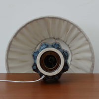 Einar JohansenがSoholm Keramikのために手掛けたモデル「1052」は、濃淡のある深いブルーグラデーションと面取りを施した立体的なフォルムが美しく、上部のマットな質感とのコントラストが上品な存在感を生む北欧ビンテージのテーブルランプです。柔らかく広がるリネンシェードの灯りが陰影豊かな陶肌をやさしく照らし、リビングや寝室のアクセントとして取り入れやすく、経年で深まった釉薬の表情が一点物ならではの味わいを引き立てています。