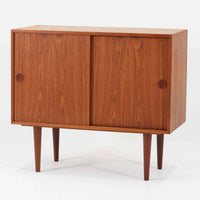 Kai Kristiansenがデザインし、Feldballes Mobelfabrikが製作した幅86cmの小ぶりなボードです。チーク材の美しい木目を活かした端正な箱型フォルムに、丸い引き手付きの引き戸がアクセントを添えます。内部には棚とトレー収納を備え、書類や小物を整理しやすい実用的な構造。すらりと伸びる脚部が軽やかさを演出し、限られた空間にも取り入れやすいサイズ感です。経年により深みを増した木肌が、北欧ビンテージならではの温もりと存在感を感じさせます。