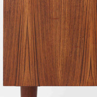 Kai Kristiansenがデザインし、Feldballes Mobelfabrikが製作した幅86cmの小ぶりなボードです。チーク材の美しい木目を活かした端正な箱型フォルムに、丸い引き手付きの引き戸がアクセントを添えます。内部には棚とトレー収納を備え、書類や小物を整理しやすい実用的な構造。すらりと伸びる脚部が軽やかさを演出し、限られた空間にも取り入れやすいサイズ感です。経年により深みを増した木肌が、北欧ビンテージならではの温もりと存在感を感じさせます。