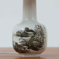 Nils Thorsson(ニルス・トールソン)によるRoyal Copenhagen(ロイヤルコペンハーゲン)の「DIANA」シリーズのテーブルランプは、白磁に繊細な草花や鳥の情景が描かれた静謐な佇まいが魅力で、淡い釉調が経年によりさらに深みを増したビンテージならではの味わいを感じさせます。柔らかく丸みを帯びたベースから伸びるすっきりとした首部のプロポーションが美しく、リネンシェードを通した穏やかな灯りが空間に上質な落ち着きを添えます。高さ32cmとコンパクトで取り入れやすく、ベッドサイドや読書灯としても活躍する、北欧陶芸の上品さが詰まった一台です。