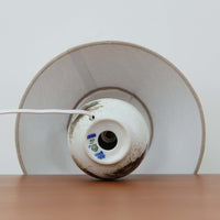 Nils Thorsson(ニルス・トールソン)によるRoyal Copenhagen(ロイヤルコペンハーゲン)の「DIANA」シリーズのテーブルランプは、白磁に繊細な草花や鳥の情景が描かれた静謐な佇まいが魅力で、淡い釉調が経年によりさらに深みを増したビンテージならではの味わいを感じさせます。柔らかく丸みを帯びたベースから伸びるすっきりとした首部のプロポーションが美しく、リネンシェードを通した穏やかな灯りが空間に上質な落ち着きを添えます。高さ32cmとコンパクトで取り入れやすく、ベッドサイドや読書灯としても活躍する、北欧陶芸の上品さが詰まった一台です。