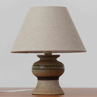 Axella製のこちらのテーブルランプは、素朴な陶土の質感と水平に重ねられた釉薬のグラデーションが生む落ち着いた佇まいが魅力で、ふくらみのある曲線的なベースと小ぶりなサイズ感が空間にさりげない温かみを添える北欧ビンテージ品です。リネンシェード越しに漏れる柔らかな灯りが陶肌の陰影をやさしく引き立て、デスクやベッドサイドなどにも取り入れやすく、経年で深まった素材の風合いが一点物ならではの味わいを感じさせてくれます。