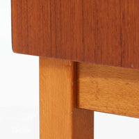 チーク材とビーチ材を組み合わせた北欧ビンテージらしい佇まいが魅力のディスプレイシェルフで、直線的で端正なフレーム構成と、木目の表情を活かした温かみのある質感が空間に落ち着きをもたらします。上部のオープン棚は器や書籍、オブジェの展示に適しており、下部には引き戸収納と引き出しを備えることで、見せる収納と隠す収納をバランス良く両立しています。脚付き構造により圧迫感が少なく、リビングやダイニング、書斎など幅広いシーンで活躍し、経年変化による色味の深まりも楽しめる一台です。