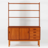 チーク材とビーチ材を組み合わせた北欧ビンテージらしい佇まいが魅力のディスプレイシェルフで、直線的で端正なフレーム構成と、木目の表情を活かした温かみのある質感が空間に落ち着きをもたらします。上部のオープン棚は器や書籍、オブジェの展示に適しており、下部には引き戸収納と引き出しを備えることで、見せる収納と隠す収納をバランス良く両立しています。脚付き構造により圧迫感が少なく、リビングやダイニング、書斎など幅広いシーンで活躍し、経年変化による色味の深まりも楽しめる一台です。