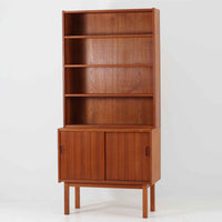 Asljunga Mobelfabrikによるディスプレイシェルフは、チーク材とビーチ材を組み合わせた端正な佇まいが魅力の北欧ビンテージ家具です。上段はオープンシェルフ構造で、棚板を活かした見せる収納が楽しめ、下段には引き戸式の収納部を備えることで実用性も確保されています。直線的で無駄のないフォルムに、掘り込み式の取っ手や脚部の軽やかなバランスが北欧らしい品の良さを添え、幅79cmの程よいサイズ感はリビングやダイニング、書斎など幅広い空間に取り入れやすく、経年変化によって深みを増した木肌と丁寧な造りが静かな存在感を放つ一台です。