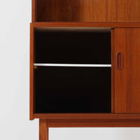 Asljunga Mobelfabrikによるディスプレイシェルフは、チーク材とビーチ材を組み合わせた端正な佇まいが魅力の北欧ビンテージ家具です。上段はオープンシェルフ構造で、棚板を活かした見せる収納が楽しめ、下段には引き戸式の収納部を備えることで実用性も確保されています。直線的で無駄のないフォルムに、掘り込み式の取っ手や脚部の軽やかなバランスが北欧らしい品の良さを添え、幅79cmの程よいサイズ感はリビングやダイニング、書斎など幅広い空間に取り入れやすく、経年変化によって深みを増した木肌と丁寧な造りが静かな存在感を放つ一台です。