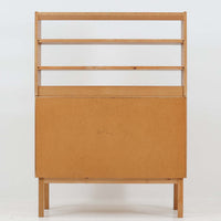 B. FridhagenがBodaforsのために手掛けたディスプレイシェルフは、端正なプロポーションと実用性を兼ね備えたスウェーデン製ビンテージ家具です。上部は抜け感のあるオープン棚構造で、器や書籍、オブジェなどを軽やかに飾ることができ、下部には4段の引き出しを備え、日常使いの収納にも対応します。オーク材ならではの明るく上品な木肌と、直線を基調とした構成が北欧らしい落ち着いた印象を生み、空間をすっきりとまとめてくれます。幅90cm、高さ122cmの小ぶりなサイズ感で、ダイニングやリビング、書斎など幅広いシーンに取り入れやすく、経年変化による木の表情も楽しめる一台です。