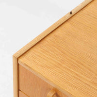 B. FridhagenがBodaforsのために手掛けたディスプレイシェルフは、端正なプロポーションと実用性を兼ね備えたスウェーデン製ビンテージ家具です。上部は抜け感のあるオープン棚構造で、器や書籍、オブジェなどを軽やかに飾ることができ、下部には4段の引き出しを備え、日常使いの収納にも対応します。オーク材ならではの明るく上品な木肌と、直線を基調とした構成が北欧らしい落ち着いた印象を生み、空間をすっきりとまとめてくれます。幅90cm、高さ122cmの小ぶりなサイズ感で、ダイニングやリビング、書斎など幅広いシーンに取り入れやすく、経年変化による木の表情も楽しめる一台です。