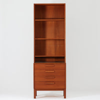 Nils Jonsson(ニールス・ヨンソン)がデザインし、Hugo Troeds(ヒューゴー・トロエッツ)社より製作されたDomi Monteシリーズのスリムシェルフです。良質なチーク材を用いた端正なキャビネットとオープンシェルフを組み合わせた構成で、収納力と見せるディスプレイ性を両立しています。直線を基調とした洗練されたフォルムと、引き出しに刻まれた繊細な手掛けが北欧らしい上品さを演出し、リビングや書斎、ダイニング収納としても活躍します。経年変化によって深みを増した木肌から、当時の職人技とビンテージならではの存在感が感じられる一台です。