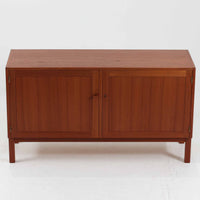 Nils JonssonがTroedsのためにデザインした「Domi Monte」モデルのキャビネットは、チーク材の豊かな木目と端正な框扉が魅力の北欧ビンテージ家具で、内部には可動棚を備えた左右対称の収納スペースが広がり食器や書類、小物類をすっきりと整理でき、チーク材をジョイントした鍵が細部の意匠性を高めつつ、直線的でシンプルな構造に細身の脚部を組み合わせることで軽やかな印象を生み出し、1960年代スウェーデン家具らしい上質で実用性の高いデザインが空間に落ち着いた存在感を添え、経年で深まった木肌の美しさも相まってリビングやダイニングのサイド収納として幅広く活躍する一台です。