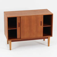 Nils Jonssonがデザインし、Hugo Troedsが製作した幅95cmの小ぶりなボードです。上質なチーク材を用いた端正な箱型フォルムに、楕円形の彫り込み取っ手がさりげないアクセントを添えています。引き戸仕様により限られた空間でも扱いやすく、内部には棚板を備え収納力も十分。すらりと伸びる脚部が軽やかな印象を与え、リビングや書斎、玄関先でも活躍します。経年により深みを増した木肌が北欧ビンテージならではの温もりと存在感を感じさせる一品です。