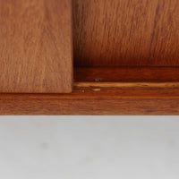 Nils Jonssonがデザインし、Hugo Troedsが製作した幅95cmの小ぶりなボードです。上質なチーク材を用いた端正な箱型フォルムに、楕円形の彫り込み取っ手がさりげないアクセントを添えています。引き戸仕様により限られた空間でも扱いやすく、内部には棚板を備え収納力も十分。すらりと伸びる脚部が軽やかな印象を与え、リビングや書斎、玄関先でも活躍します。経年により深みを増した木肌が北欧ビンテージならではの温もりと存在感を感じさせる一品です。