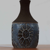 Chris HaslevがJetiのために手掛けたこちらのテーブルランプは、太陽を思わせるレリーフ模様をまとった陶器ベースと、素朴な土肌と釉薬の濃淡が織りなす豊かな表情が魅力で、コンパクトながら存在感を放つ北欧ビンテージ品です。上部のマットな質感が造形を引き締め、リネンシェード越しに広がるあたたかな灯りが空間をやさしく包み込み、リビングやベッドサイドのアクセントとして取り入れやすい一台に仕上がっています。