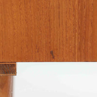 デンマークで製作されたチーク材のローボードです。幅100cmの小ぶりなサイズながら、温かみのある木目とシンプルな直線的フォルムが北欧らしい落ち着いた佇まいを演出します。前面には手掛け付きのスライド扉が備えられ、内部収納をすっきりと隠しながら使いやすさも確保。細身の脚部が軽やかな印象を与え、リビングや玄関、ベッドサイドなど様々な空間で活躍します。背板には壁掛け用の金具が取り付けられており、収納内部にはDIYによる木材の追加や小さな穴が見られますが、ビンテージ品ならではの味わいとして楽しめる一台です。