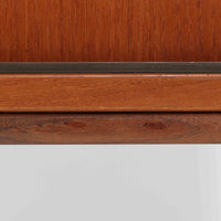 デンマークで製作されたチーク材のローボードです。幅100cmの小ぶりなサイズながら、温かみのある木目とシンプルな直線的フォルムが北欧らしい落ち着いた佇まいを演出します。前面には手掛け付きのスライド扉が備えられ、内部収納をすっきりと隠しながら使いやすさも確保。細身の脚部が軽やかな印象を与え、リビングや玄関、ベッドサイドなど様々な空間で活躍します。背板には壁掛け用の金具が取り付けられており、収納内部にはDIYによる木材の追加や小さな穴が見られますが、ビンテージ品ならではの味わいとして楽しめる一台です。