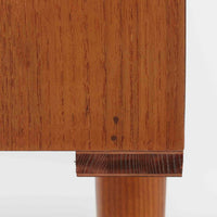 デンマークで製作されたチーク材のローボードです。幅100cmの小ぶりなサイズながら、温かみのある木目とシンプルな直線的フォルムが北欧らしい落ち着いた佇まいを演出します。前面には手掛け付きのスライド扉が備えられ、内部収納をすっきりと隠しながら使いやすさも確保。細身の脚部が軽やかな印象を与え、リビングや玄関、ベッドサイドなど様々な空間で活躍します。背板には壁掛け用の金具が取り付けられており、収納内部にはDIYによる木材の追加や小さな穴が見られますが、ビンテージ品ならではの味わいとして楽しめる一台です。