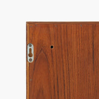 デンマークで製作されたチーク材のローボードです。幅100cmの小ぶりなサイズながら、温かみのある木目とシンプルな直線的フォルムが北欧らしい落ち着いた佇まいを演出します。前面には手掛け付きのスライド扉が備えられ、内部収納をすっきりと隠しながら使いやすさも確保。細身の脚部が軽やかな印象を与え、リビングや玄関、ベッドサイドなど様々な空間で活躍します。背板には壁掛け用の金具が取り付けられており、収納内部にはDIYによる木材の追加や小さな穴が見られますが、ビンテージ品ならではの味わいとして楽しめる一台です。