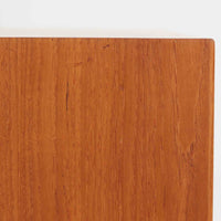 デンマークで製作されたチーク材のローボードです。幅100cmの小ぶりなサイズながら、温かみのある木目とシンプルな直線的フォルムが北欧らしい落ち着いた佇まいを演出します。前面には手掛け付きのスライド扉が備えられ、内部収納をすっきりと隠しながら使いやすさも確保。細身の脚部が軽やかな印象を与え、リビングや玄関、ベッドサイドなど様々な空間で活躍します。背板には壁掛け用の金具が取り付けられており、収納内部にはDIYによる木材の追加や小さな穴が見られますが、ビンテージ品ならではの味わいとして楽しめる一台です。