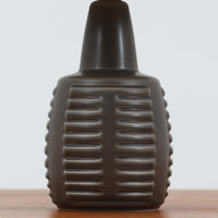 Rigmor Nielsenがデザインし、Soholm Keramikが手掛けたテーブルランプです。高さ37cmの取り入れやすいサイズに、艶やかな陶磁器ベースとナチュラルなリネンシェードを組み合わせた、落ち着きある北欧ビンテージらしい一台。ベースには規則的な立体リブ装飾が施され、陰影豊かな表情と彫刻的な存在感を生み出しています。点灯時にはシェード越しの柔らかな光が釉薬の奥行きや貫入の表情を引き立て、チェストやサイドテーブル、ベッドサイドに穏やかな雰囲気を演出。Rigmor Nielsenらしい造形美とSoholmの高い陶芸技術が感じられる、希少性の高いビンテージ照明です。