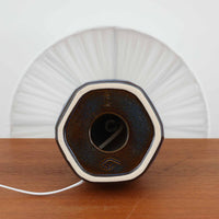 Einar Johansenデザイン、Soholm Keramik製モデル1020のデンマーク製テーブルランプです。深みのあるコバルトブルーの陶磁器ベースは、静かな艶を湛えた釉薬の美しさと、角をやわらかく落とした多面体フォルムが印象的で、正面にあしらわれた小さなメダリオン装飾がさりげないアクセントになっています。すっと伸びるネックと安定感あるベースのバランスが美しく、プリーツ状のリネンシェードを通した柔らかな灯りが空間に上品な陰影を演出。サイドボードやベッドサイド、コンソール上の間接照明として使いやすく、北欧ビンテージらしい洗練と温もりを兼ね備えた一台です。経年により艶を増した青釉の豊かな表情が、コレクタブルな魅力をいっそう高めています。