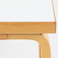Alvar Aaltoがデザインし、Artekが製作したモデル81Cの正方形ダイニングテーブルです。バーチ材のしなやかな曲木脚とホワイトラミネート天板の組み合わせが、アアルトらしい機能美と軽やかな佇まいを生み出しています。幅75cmの扱いやすいサイズは2人用のダイニングテーブルとしてはもちろん、ワークデスクやショップ什器としても取り入れやすい一台。経年により深みを増した木肌と、長年使い込まれた天板の風合いがビンテージならではの味わいを感じさせ、Artekの普遍的なデザイン性と希少な北欧オリジナルの存在感を空間に添えてくれます。