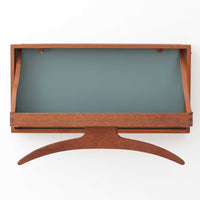 Adam Hoff & Poul Ostergaardがデザインし、Virum Mobelsnickeriにより製作された「The Hanger」ハンガーラックです。チーク材の温かみある木目と、優雅な曲線を描くベースのフォルムが印象的なデザイン。内部にはフックが備えられ、コートや帽子などを掛けて収納できます。フロントのフラップを開くとハンガー部分が現れる機能的な構造で、使用しないときはすっきりとした壁面収納として美しく収まります。革ベルトによる固定や細部の造りにも職人技が感じられる、北欧ビンテージならではの洗練された一品です。