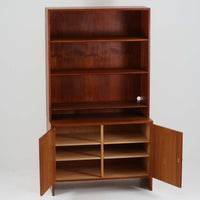 Hans J. Wegnerがデザインし、Ry Moblerが製作したディスプレイシェルフです。美しい木目をもつチーク材を主体に、内部や構造部にはオーク材、金具には真鍮を組み合わせた上質なつくりが魅力。上部のオープン棚は飾り棚として器やオブジェ、本を美しく見せ、下部の開き戸収納は細かい日用品や書類をすっきり隠して収納できます。直線的で端正なフォルムの中に、ウェグナーらしい丁寧な木工技術と素材の美しさが息づき、経年で深みを増した色艶が空間に格別の存在感を添える一品です。リビングや書斎、ショップ什器としてもおすすめです。