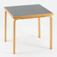 Alvar Aaltoがデザインし、Artekより製作された「81C」ダイニングテーブルです。バーチ材を用いたフレームに、天板には落ち着いた質感のリノリウムを組み合わせたシンプルで機能的なデザインが特徴。脚部にはアアルトを象徴するL字型の曲木構造が採用されており、軽やかで柔らかな印象を与えます。幅75cmの正方形サイズはダイニングはもちろんワークテーブルとしても使いやすく、日常の空間に北欧デザインの美しさと実用性をもたらすビンテージ家具です。本個体は、脚部の5枚レイヤー構造、1973年以降に採用されたプラスネジ、および天板裏の3段構成スタンプの仕様から、1973年~1990年代始めに掛けて製造されたと思われます。