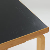 Alvar Aaltoがデザインし、Artekより製作された「81C」ダイニングテーブルです。バーチ材を用いたフレームに、天板には落ち着いた質感のリノリウムを組み合わせたシンプルで機能的なデザインが特徴。脚部にはアアルトを象徴するL字型の曲木構造が採用されており、軽やかで柔らかな印象を与えます。幅75cmの正方形サイズはダイニングはもちろんワークテーブルとしても使いやすく、日常の空間に北欧デザインの美しさと実用性をもたらすビンテージ家具です。本個体は、脚部の5枚レイヤー構造、1973年以降に採用されたプラスネジ、および天板裏の3段構成スタンプの仕様から、1973年~1990年代始めに掛けて製造されたと思われます。