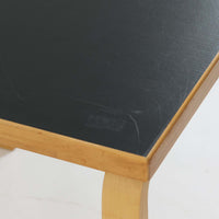 Alvar Aaltoがデザインし、Artekより製作された「81C」ダイニングテーブルです。バーチ材を用いたフレームに、天板には落ち着いた質感のリノリウムを組み合わせたシンプルで機能的なデザインが特徴。脚部にはアアルトを象徴するL字型の曲木構造が採用されており、軽やかで柔らかな印象を与えます。幅75cmの正方形サイズはダイニングはもちろんワークテーブルとしても使いやすく、日常の空間に北欧デザインの美しさと実用性をもたらすビンテージ家具です。本個体は、脚部の5枚レイヤー構造、1973年以降に採用されたプラスネジ、および天板裏の3段構成スタンプの仕様から、1973年~1990年代始めに掛けて製造されたと思われます。