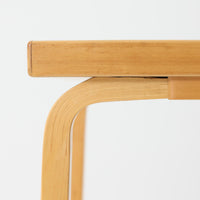 Alvar Aaltoがデザインし、Artekより製作された「81C」ダイニングテーブルです。バーチ材を用いたフレームに、天板には落ち着いた質感のリノリウムを組み合わせたシンプルで機能的なデザインが特徴。脚部にはアアルトを象徴するL字型の曲木構造が採用されており、軽やかで柔らかな印象を与えます。幅75cmの正方形サイズはダイニングはもちろんワークテーブルとしても使いやすく、日常の空間に北欧デザインの美しさと実用性をもたらすビンテージ家具です。本個体は、脚部の5枚レイヤー構造、1973年以降に採用されたプラスネジ、および天板裏の3段構成スタンプの仕様から、1973年~1990年代始めに掛けて製造されたと思われます。
