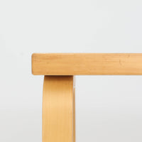 Alvar Aaltoがデザインし、Artekより製作された「81C」ダイニングテーブルです。バーチ材を用いたフレームに、天板には落ち着いた質感のリノリウムを組み合わせたシンプルで機能的なデザインが特徴。脚部にはアアルトを象徴するL字型の曲木構造が採用されており、軽やかで柔らかな印象を与えます。幅75cmの正方形サイズはダイニングはもちろんワークテーブルとしても使いやすく、日常の空間に北欧デザインの美しさと実用性をもたらすビンテージ家具です。本個体は、脚部の5枚レイヤー構造、1973年以降に採用されたプラスネジ、および天板裏の3段構成スタンプの仕様から、1973年~1990年代始めに掛けて製造されたと思われます。