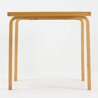 Alvar Aaltoがデザインし、Artekより製作された「81C」ダイニングテーブルです。バーチ材を用いたフレームに、天板には落ち着いた質感のリノリウムを組み合わせたシンプルで機能的なデザインが特徴。脚部にはアアルトを象徴するL字型の曲木構造が採用されており、軽やかで柔らかな印象を与えます。幅75cmの正方形サイズはダイニングはもちろんワークテーブルとしても使いやすく、日常の空間に北欧デザインの美しさと実用性をもたらすビンテージ家具です。本個体は、脚部の5枚レイヤー構造、1973年以降に採用されたプラスネジ、および天板裏の3段構成スタンプの仕様から、1973年~1990年代始めに掛けて製造されたと思われます。