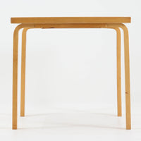 Alvar Aaltoがデザインし、Artekより製作された「81C」ダイニングテーブルです。バーチ材を用いたフレームに、天板には落ち着いた質感のリノリウムを組み合わせたシンプルで機能的なデザインが特徴。脚部にはアアルトを象徴するL字型の曲木構造が採用されており、軽やかで柔らかな印象を与えます。幅75cmの正方形サイズはダイニングはもちろんワークテーブルとしても使いやすく、日常の空間に北欧デザインの美しさと実用性をもたらすビンテージ家具です。本個体は、脚部の5枚レイヤー構造、1973年以降に採用されたプラスネジ、および天板裏の3段構成スタンプの仕様から、1973年~1990年代始めに掛けて製造されたと思われます。