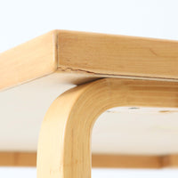 Alvar Aaltoがデザインし、Artekより製作された「81C」ダイニングテーブルです。バーチ材を用いたフレームに、天板には落ち着いた質感のリノリウムを組み合わせたシンプルで機能的なデザインが特徴。脚部にはアアルトを象徴するL字型の曲木構造が採用されており、軽やかで柔らかな印象を与えます。幅75cmの正方形サイズはダイニングはもちろんワークテーブルとしても使いやすく、日常の空間に北欧デザインの美しさと実用性をもたらすビンテージ家具です。本個体は、脚部の5枚レイヤー構造、1973年以降に採用されたプラスネジ、および天板裏の3段構成スタンプの仕様から、1973年~1990年代始めに掛けて製造されたと思われます。