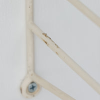 Nils Strinningがデザインし、String Design ABが製造したチーク材のウォールシェルフです。細身の金属製サイドフレームに3枚の木製棚板を組み合わせた軽快な構成で、圧迫感を抑えながら書籍や器、オブジェなどを美しく飾ることができます。棚板の位置を調整しやすい機能的な構造と、直線的で無駄のない造形は北欧らしい合理性を感じさせ、チーク材の経年による深い色合いと金属フレームの対比も魅力。リビングや書斎、店舗空間の壁面を有効に使える存在感ある一台です。