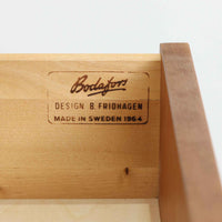 B. Fridhagenがデザインし、Bodaforsが製造したチーク材のディスプレイシェルフです。上部には背板のない開放的な棚を備え、書籍や器、オブジェなどを軽やかに飾れる構成。下部には4杯の引出しを組み合わせ、見せる収納と隠す収納を一台で使い分けられます。細身のフレームや直線的な脚部、縦に配した小ぶりな取手など、端正な職人技が感じられる佇まいも魅力。経年によって深みを増した木肌が、リビングや書斎、店舗空間に温かな存在感を添える一台です。