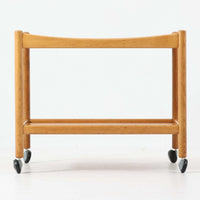 Hans J. Wegnerがデザインし、PP Moblerが製造したAT45のキャスターワゴンです。明るく温かなオーク材を用い、上下2段の棚板と四隅のキャスターを組み合わせた、移動性に優れた実用的な構成が特徴。上段には持ち手を兼ねる開口部が設けられ、緩やかに湾曲する側板や丸みのある支柱など、ウェグナーらしい柔らかな造形と丁寧な木工技術が感じられます。経年によって深まった木肌を楽しみながら、キッチンやダイニング、リビングで配膳や収納に活躍する一台です。