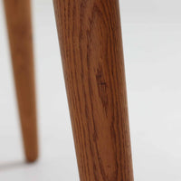 Hans J. Wegnerがデザインし、Andreas Tuckが製造を手掛けたAT8。チーク材の円形天板とオーク材の脚部を組み合わせ、異なる木材の表情を巧みに生かした一台です。直径98cmの伸びやかな天板を、外側へ緩やかに開く4本のテーパードレッグが軽快に支えるシンプルな構成で、素材とプロポーションの美しさが際立ちます。ソファを囲むリビングの主役として取り入れやすく、ウェグナーらしい端正な造形と年月を重ねた木部の風合いを味わえるビンテージ品です。