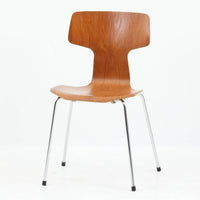 アルネ・ヤコブセンがデザインし、Fritz Hansenが製造した「T Chair」です。チーク材の成形合板による背座一体型のシェルは、背面上部を左右に広げた特徴的なシルエットと、身体に沿う緩やかな曲面が魅力。細身の金属脚との組み合わせが軽快で、ダイニングはもちろん、書斎や玄関のアクセントチェアにもおすすめです。美しい木目と時を重ねた風合い、合理的な構造に宿る北欧ビンテージらしい存在感を楽しめます。