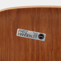 アルネ・ヤコブセンがデザインし、Fritz Hansenが製造した「T Chair」です。チーク材の成形合板による背座一体型のシェルは、背面上部を左右に広げた特徴的なシルエットと、身体に沿う緩やかな曲面が魅力。細身の金属脚との組み合わせが軽快で、ダイニングはもちろん、書斎や玄関のアクセントチェアにもおすすめです。美しい木目と時を重ねた風合い、合理的な構造に宿る北欧ビンテージらしい存在感を楽しめます。