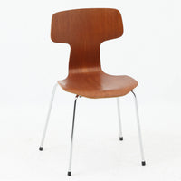 アルネ・ヤコブセンがデザインし、Fritz Hansenが製造した「T Chair」です。チーク材の成形合板による背座一体型のシェルは、背面上部を左右に広げた特徴的なシルエットと、身体に沿う緩やかな曲面が魅力。細身の金属脚との組み合わせが軽快で、ダイニングはもちろん、書斎や玄関のアクセントチェアにもおすすめです。美しい木目と時を重ねた風合い、合理的な構造に宿る北欧ビンテージらしい存在感を楽しめます。