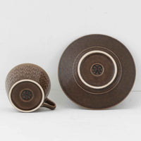 デンマークを代表するデザイナー、イェンス・H・クイストゴーによる「Azur(アズール)」シリーズのヴィンテージカッププ&ソーサーです。1960年代にKronjydenから制作が始まったシリーズは、その後Nissen、Bing&Grondahlと引き継がれ長く愛されたシリーズとなりました。落ち着いたブラウンとプラム色の繊細なフラワーレリーフが施されたストーンウェアは、自然の美しさを食卓にそっと運びます。特にAzurシリーズはヴィンテージ市場でも流通量が極めて少なく高価な逸品となります。