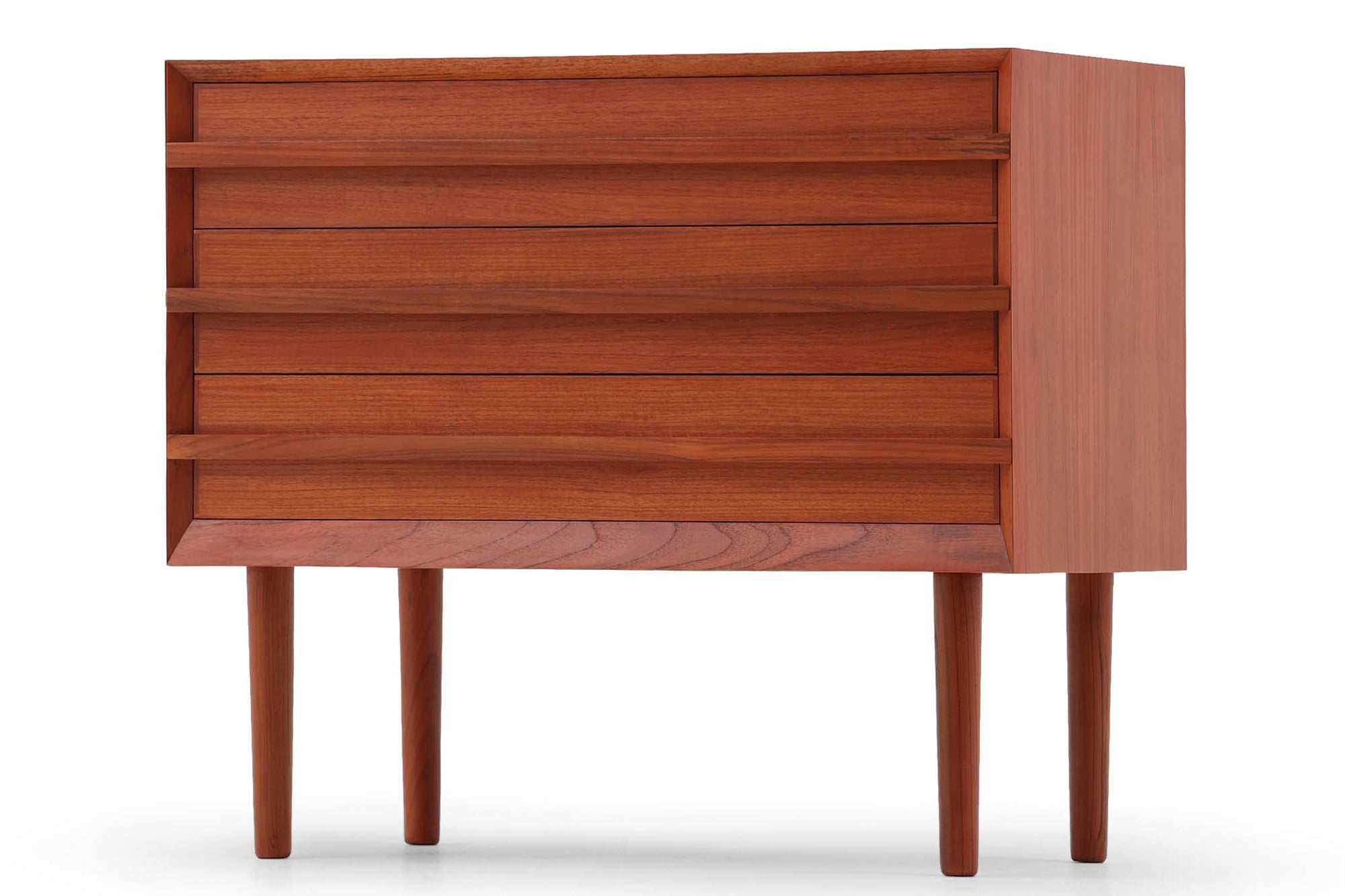 チーク材の３段チェストです。刃物のようなデザインの取っ手がチェスト本体と一体化することで収納時、非常にモダンで美しい印象を与えます。またこちらの長い取っ手は開け閉め時、ストレス無く、使い勝手がよいのも特徴です。チェスト本体の外枠が正面に対してフラットではなく斜めになっているなど高級感のあるデザインに仕上げています。