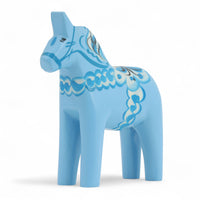 Grannas A. Olsson Hemslojd（グランナス オルソン ヘムスロイド）は、1922年にスウェーデン・ダーラナ地方ヌスナスで創業した世界最古のダラホース工房です。創業者のアンダース オルソン氏は、当初家族経営のパン屋から木工品製造へと転換し、弟らと協力してダラホースの生産を始めました。ひとつずつ選別されたスロースギ材（シルヤン湖周辺の赤松）を使い、木型の挽きから手彫り、下地塗装、さらに熟練のリップル（波模様）ペインターによるフリーハンド装飾を施します。その後、丁寧にニス仕上げされ、赤や白、青など伝統色に彩られた馬たちは、まさに「スウェーデンの象徴」として世界中の家庭や店舗に愛されています。伝統工房としての格式を受け継ぎつつも、パステルやモノトーン、限定柄などを加えることで、現代のインテリアにもマッチするデザイン性も追求しています。